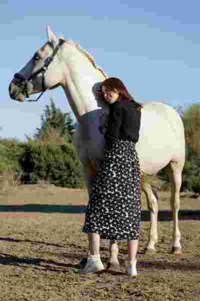 Modèle en jupe fleurie noir et blanc appuyée contre un cheval blanc — Lookbook April & C, Occitanie
