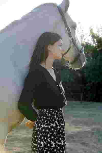 Modèle de profil en cardigan noir face à un cheval blanc au coucher du soleil — Lookbook April & C, Occitanie
