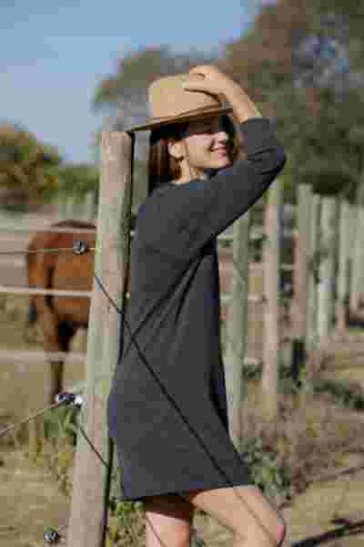 Modèle en robe grise et chapeau de paille appuyée contre un poteau, chevaux en arrière-plan — Lookbook April & C, Montpellier