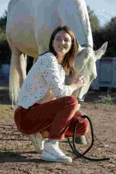 Modèle accroupie en blouse broderie anglaise et pantalon terracotta avec un cheval blanc — Lookbook April & C, Occitanie