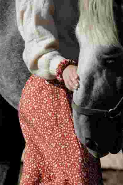 Détail jupe longue fleurie terracotta et main qui caresse un cheval gris - Lookbook April & C, Occitanie