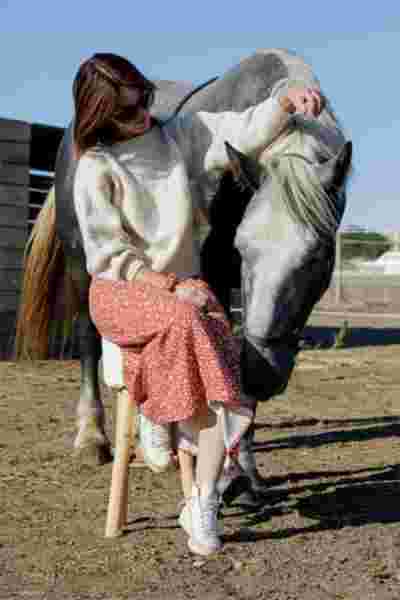 Modèle assise sur un tabouret en jupe fleurie et pull écru, complicité avec un cheval gris — Photographe lookbook mode Montpellier, April & C