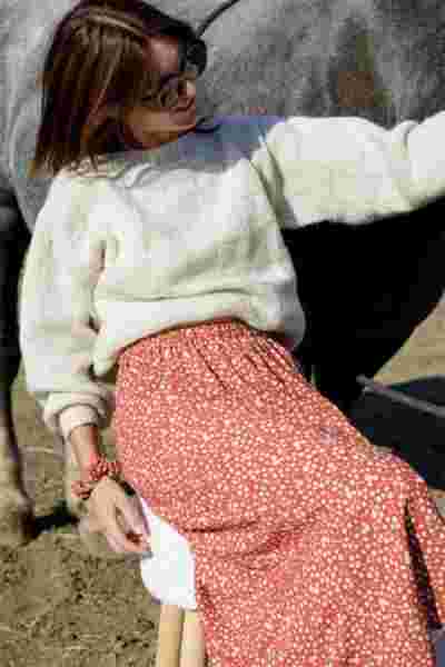 Portrait modèle souriante en pull écru et jupe fleurie terracotta avec cheval — Lookbook April & C, Occitanie