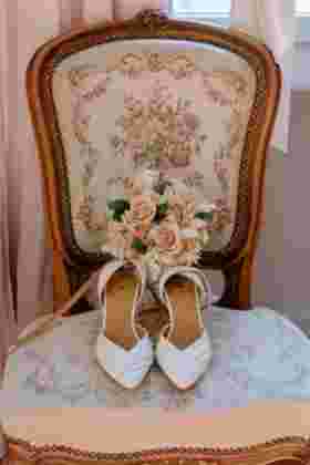 Chaussures blanches de mariée et bouquet de roses posés sur un fauteuil — Mariage Château Le Bouïs, Gruissan