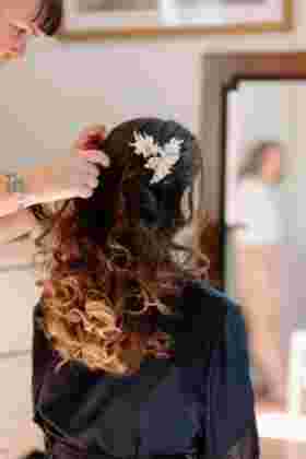 Coiffeuse ajustant l'accessoire fleuri dans les cheveux bouclés de la mariée — Préparatifs mariage Gruissan, Occitanie