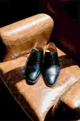 Détail chaussures noires du marié posées sur un fauteuil en cuir — Mariage Château Le Bouïs