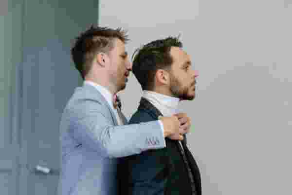 Témoin ajustant le col et la cravate du marié avant la cérémonie — Mariage Château Le Bouïs, Occitanie