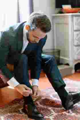 Marié enfilant ses chaussures noires sur un tapis lors des préparatifs — Mariage Château Le Bouïs, Gruissan