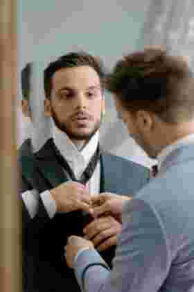 Marié se regardant dans le miroir pendant que son témoin ajuste sa cravate — Mariage Gruissan, Occitanie